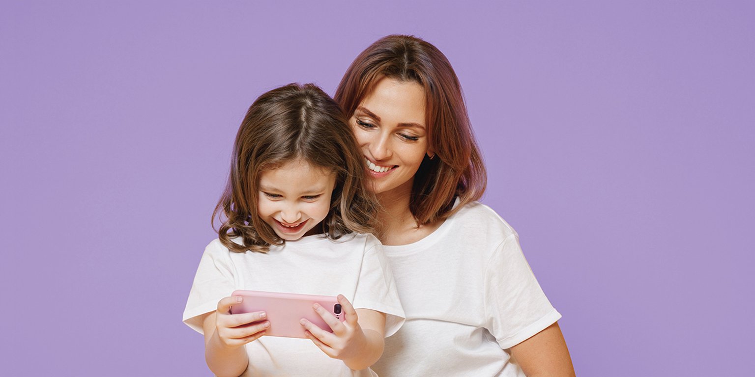 Mutter und Tochter schauen gemeinsam auf ein Smartphone und lächeln.